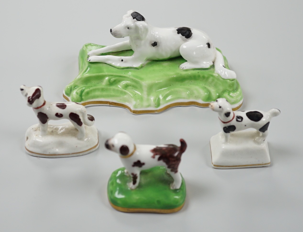 Three toy Staffordshire models of standing terriers; two with brown spots and the other black spots, together with a small Staffordshire model of a recumbent black and white setter on modelled base. c.1830-50, Largest 13